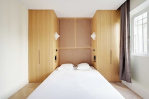 A bedroom with a bed, two bedside tables, a window with curtains, and wooden wardrobe units. - Modern a/c - 1bdr/4p Flat - Montorgueil (Paris)