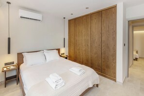 A hotel room with a large bed, wooden wardrobe, bedside tables, and an air conditioning unit. - Chic Athenian Riviera Retreat in Vari by GHH (Vari)