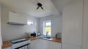 Uma cozinha compacta com armários brancos, fogão a gás, micro-ondas e pia.