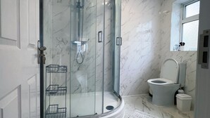 Um banheiro moderno com chuveiro em box de vidro, vaso sanitário e piso de mármore.