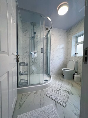 Ein modernes Badezimmer mit einer gläsernen Dusche, einer Toilette und Marmorböden.