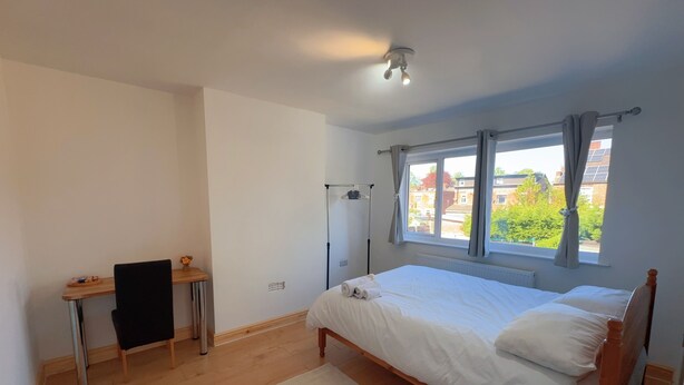 Quarto com uma cama de solteiro, escrivaninha, cadeira, radiador e janela com cortinas.
