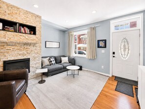 A living room with a fireplace, a sofa, a coffee table, and a bookshelf. - 2BR/2.5BA Stylish home near Center City + King Bed (Philadelphia)