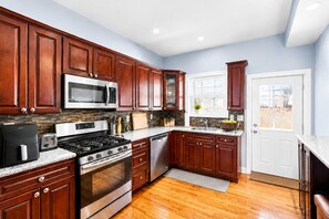A modern kitchen with wooden cabinets, stainless steel appliances, and a view to the outside. - 2BR/2.5BA Stylish home near Center City + King Bed (Philadelphia)