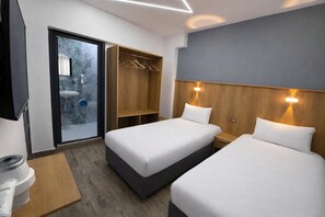 Habitación de hotel con dos camas, un armario de madera, un espejo, un lavamanos y una puerta corrediza de vidrio al exterior.