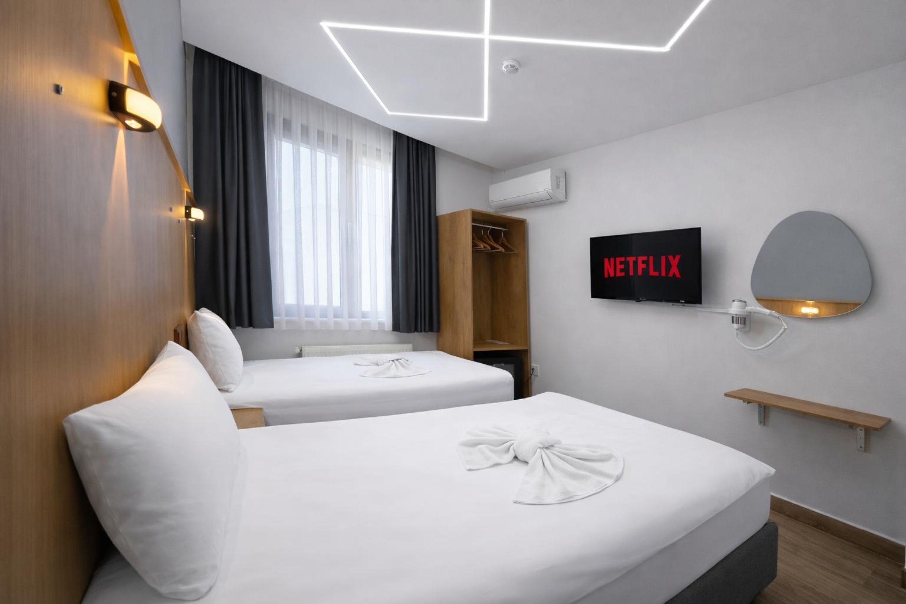 A hotel room with two beds, a wardrobe, a TV, and a mirror.