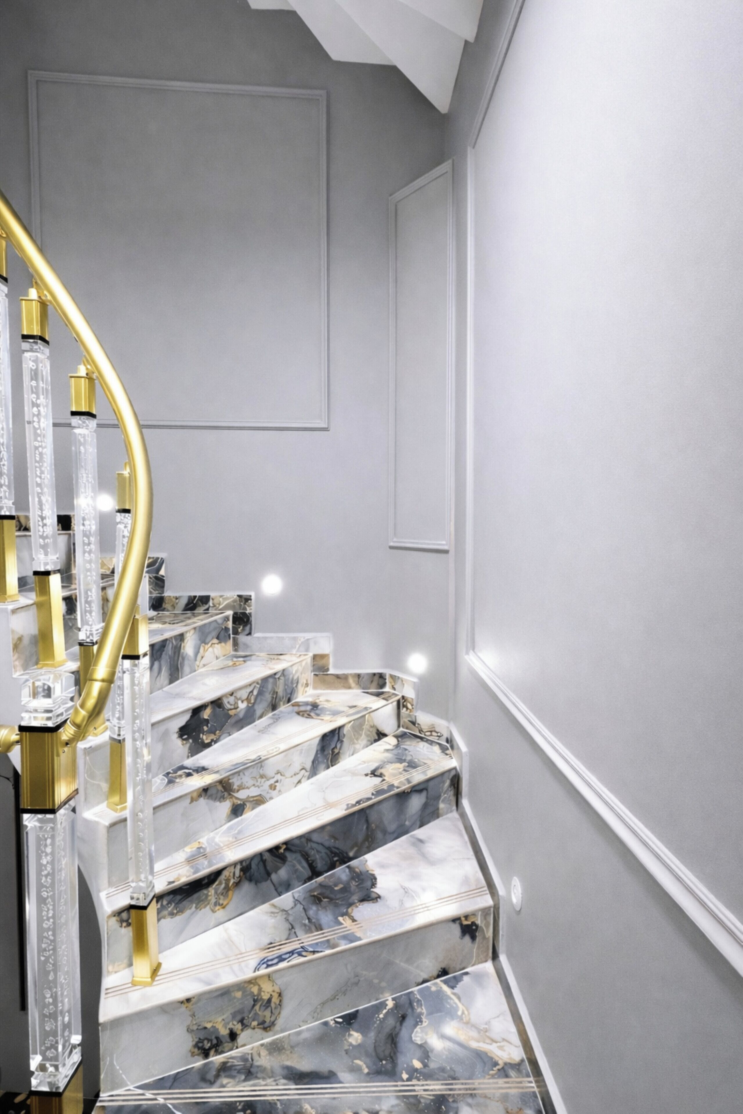 A marble staircase with a golden spiral railing and clear glass panels.