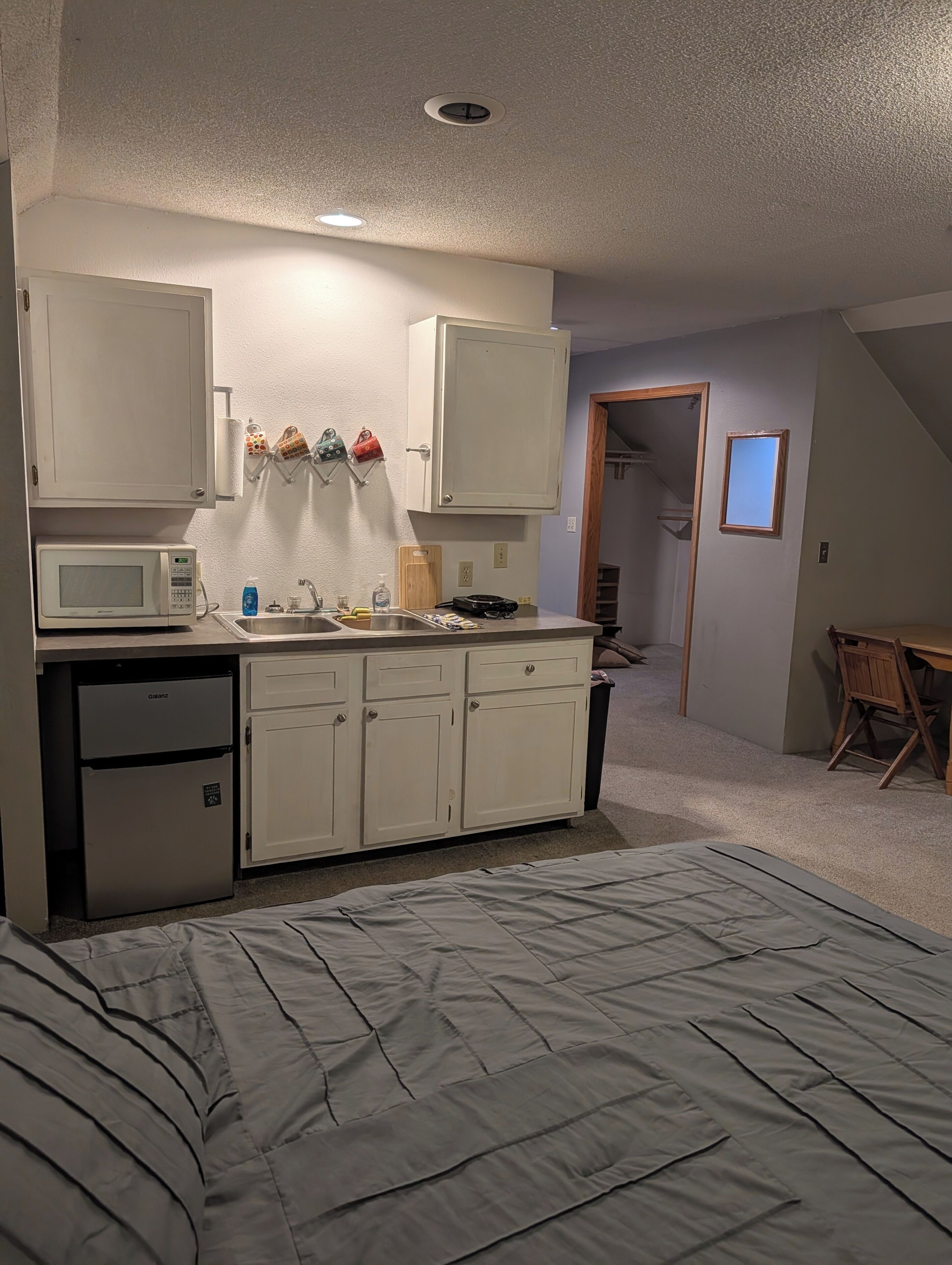 A compact bedroom with a bed, kitchenette, and a small bathroom.