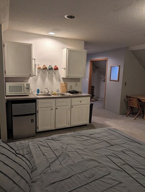 A compact bedroom with a bed, kitchenette, and a small bathroom. - Adorable studio with AC in charming Winfield (Winfield)