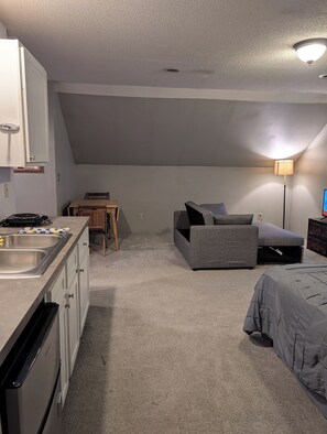 A compact room with a kitchenette, a sofa, a small table, and a lamp. - Adorable studio with AC in charming Winfield (Winfield)