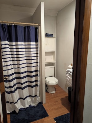 A bathroom with a shower curtain, toilet, and storage cabinets. - Adorable studio with AC in charming Winfield (Winfield)