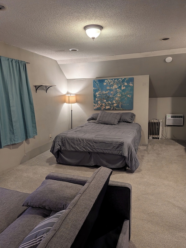 A bedroom with a bed, a standing lamp, a radiator, and a painting on the wall. - Adorable studio with AC in charming Winfield (Winfield)