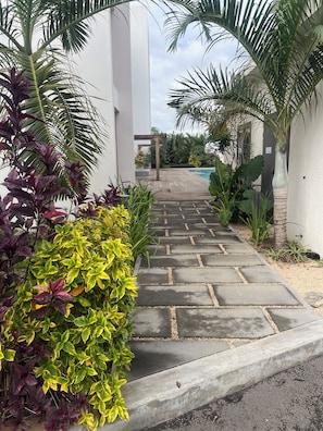A pathway leading to a pool area with a pergola, surrounded by lush greenery and a modern building. - Premium Apartment - Pool - 10-minute walk to the beach - PEREYBERE, MAURITIUS (pereybère)