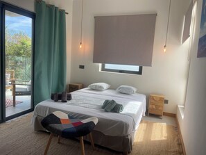 A bedroom with a bed, a chair, a window with a blind, bedside tables, and a view of the outdoors. - Premium Apartment - Pool - 10-minute walk to the beach - PEREYBERE, MAURITIUS (pereybère)
