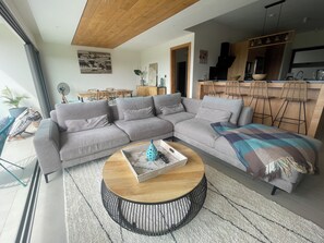 Ein modernes Wohnzimmer mit einem Ecksofa, einem runden Couchtisch und einer Küchenzeile mit Barhocker.