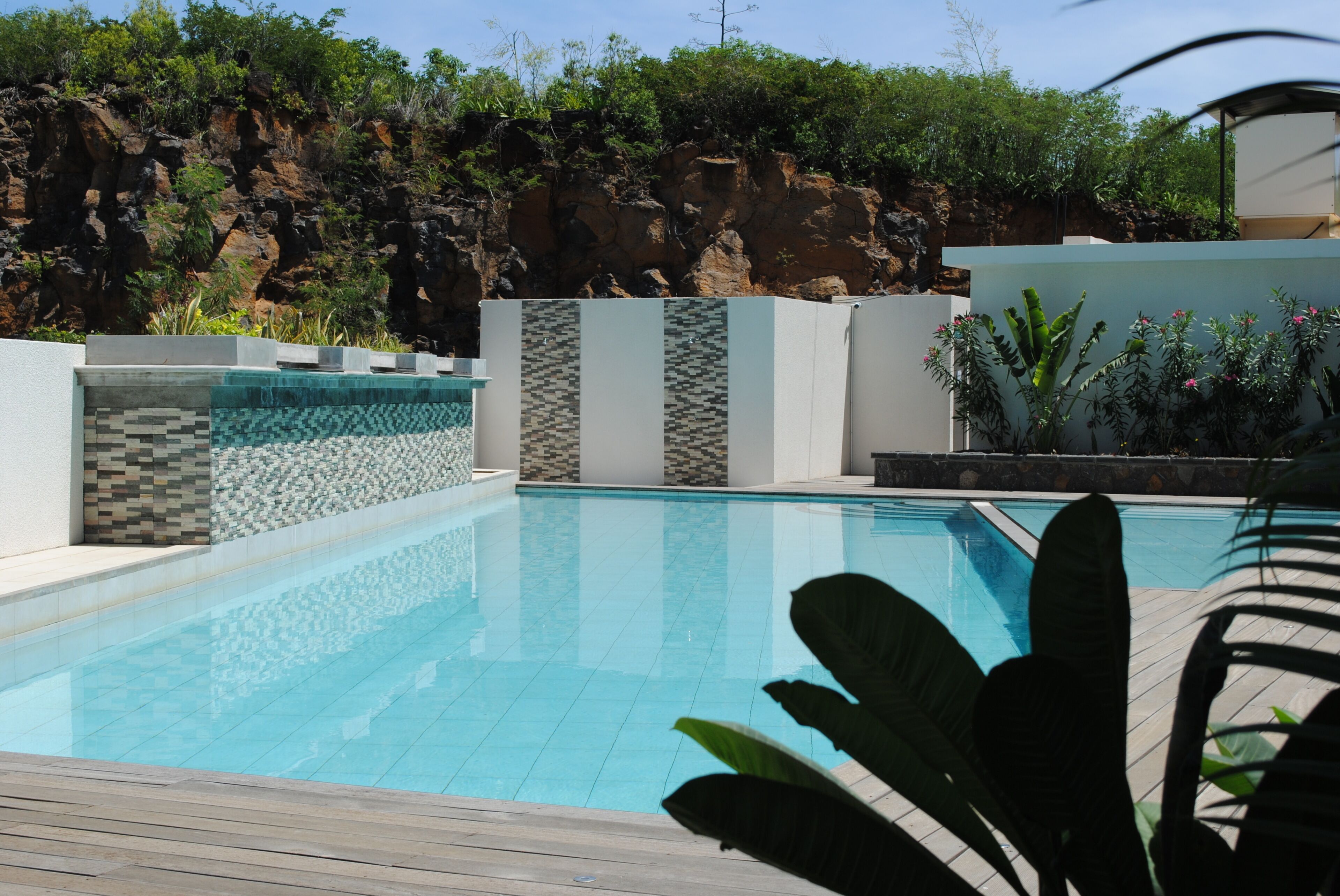 Une piscine dotée d’une terrasse en bois, de murs carrelés et surplombant une falaise rocheuse.