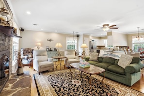 A spacious living room with a green sofa, a coffee table, and a fireplace. There is a kitchen area with a refrigerator and a dining table. - Massanutten Foliage | Game Room &Screened-in Porch (McGaheysville)