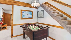 Ett rum med ett fotbollsspel, synliga träbjälkar, en trappa och en kristallkrona.