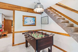 Ein Zimmer mit Tischfußball, Holzbalken, einer Treppe und einer Kandelaberleuchte.