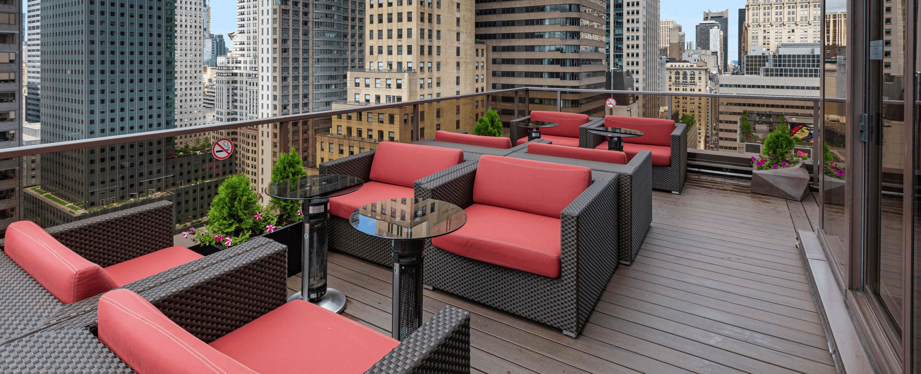 A rooftop terrace with wicker furniture, a round table, and potted plants.
