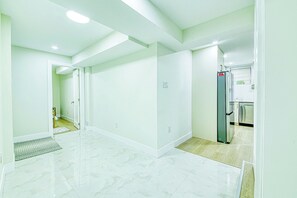 A spacious, well-lit room with a marble floor, a kitchen area with modern appliances, and a door leading to another room. - Luxury 3BR Suite | EV Charger | Long Stays (Hamilton)
