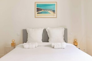 Ein Hotelzimmer mit einem Bett, zwei Kissen, einem gerahmten Bild an der Wand und zwei Nachttischen mit Lampen.