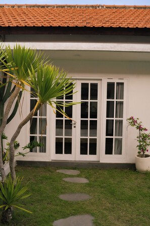 Une maison avec un toit en tuiles, des murs extérieurs blancs et un petit jardin agrémenté d’un palmier et d’une plante en pot.