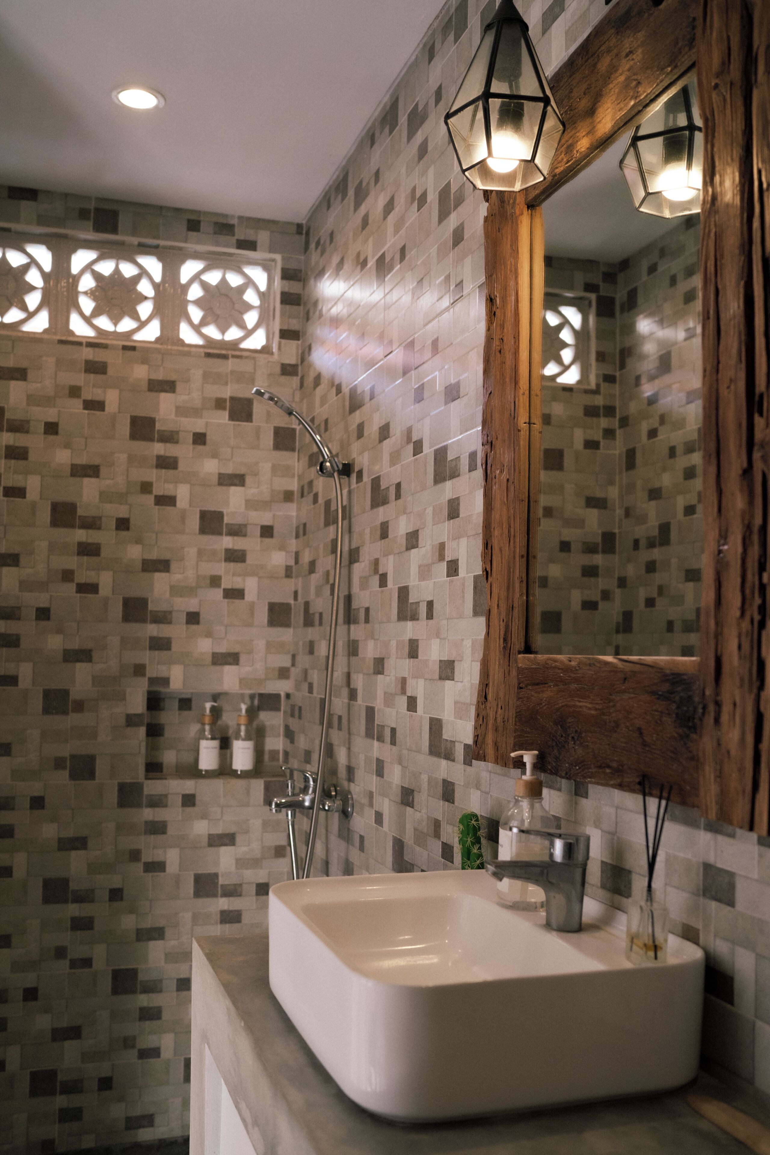 Ein Badezimmer mit gefliesten Wänden, einem spiegelnden Holzbettrahmen, einer Dusche und einem Waschbecken mit Seifenspender.