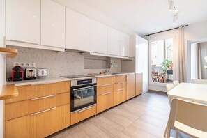 A modern kitchen with white cabinets, a built-in oven, and a dining area with a table and chairs. - Terrace Apartment in Heart of St-Germain-des-Prés (Paris)