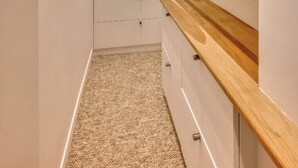 Ein schmaler Flur mit weißen Wänden, einem Teppichboden und Regalen aus Holz auf der rechten Seite.