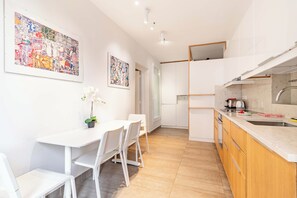 Une cuisine moderne avec des meubles blancs, un coin repas avec des chaises blanches et un grand tableau abstrait accroché au mur.