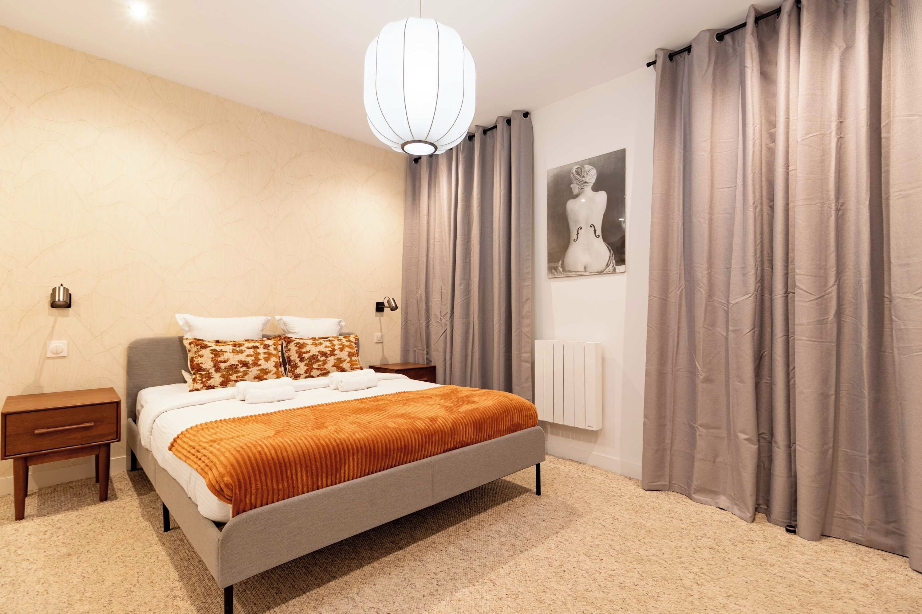 A bedroom with a bed, nightstands, a radiator, and a painting on the wall.