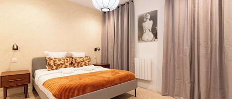 A bedroom with a bed, nightstands, a radiator, and a painting on the wall.