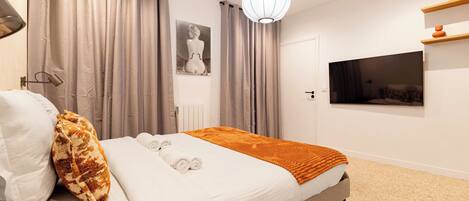 A modern bedroom with a bed, curtains, a wall-mounted TV, and a ceiling light.