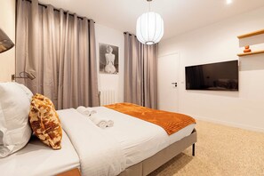 Une chambre à coucher moderne avec un lit, des rideaux, un téléviseur fixé au mur et un luminaire au plafond.