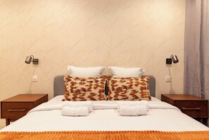A neatly made bed with white linens and two patterned pillows, flanked by two bedside tables with lamps, against a textured wall. - Terrace Apartment in Heart of St-Germain-des-Prés (Paris)