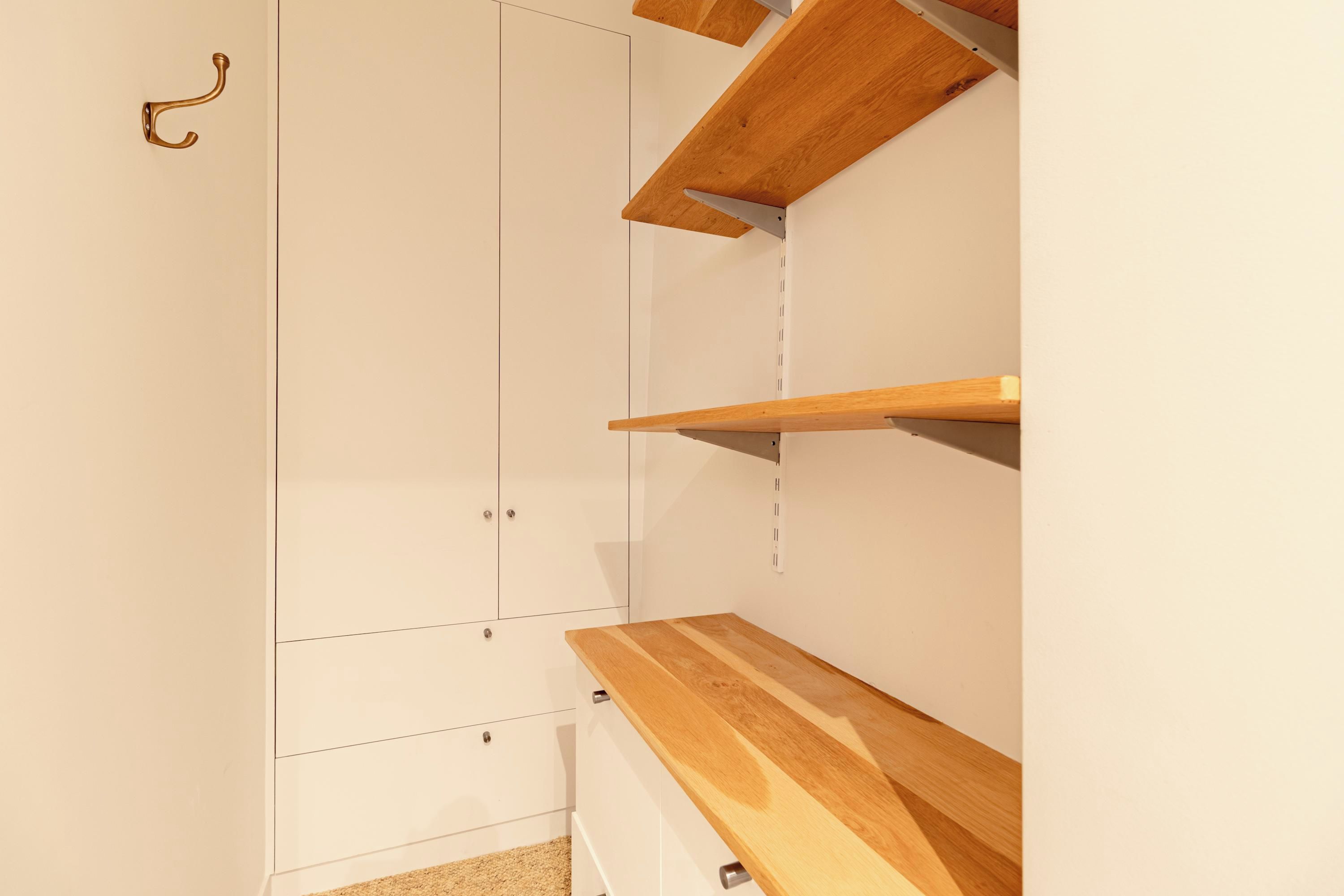 A room with a white wardrobe, wooden shelves, and a hook on the wall.