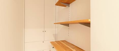 A room with a white wardrobe, wooden shelves, and a hook on the wall.
