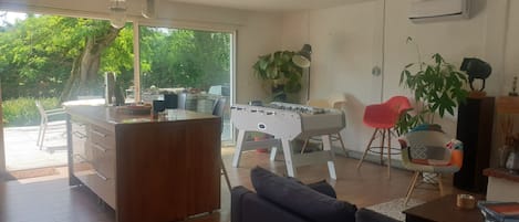 A living room with a foosball table, a sofa, and a dining area with a table and chairs.