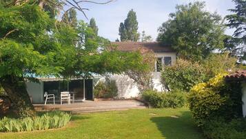 A residential property with a garden, a patio with outdoor furniture, and a white building with a tiled roof.