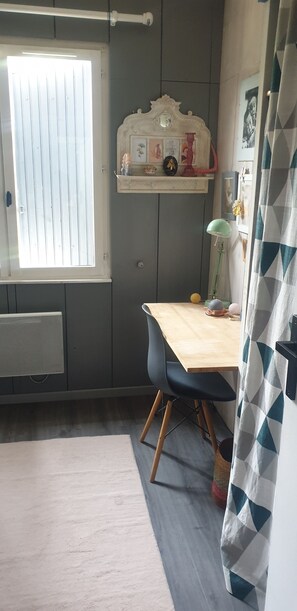 A room with a wooden table, a chair, a radiator, a window with blinds, a shelf with decorative items, and a curtain. - House with a pool, pool table, foosball table, and ping-pong table. (Villemur-sur-Tarn)