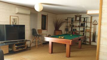 Una habitación con mesa de billar, televisión, estantería y una silla.