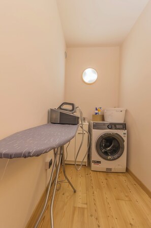 A laundry room with a washing machine, an iron, and a small round mirror on the wall. - La Corte dei Laghi. Luxury homestay in the heart of the Italian Lake District. (Pusiano)