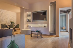 A modern living room with a flat-screen TV mounted on the wall, a dining area with chairs and a table, and a hallway leading to another room. - La Corte dei Laghi. Luxury homestay in the heart of the Italian Lake District. (Pusiano)