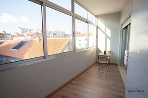 Ein Balkon mit großen Fenstern, einem kleinen Tisch und einem Stuhl.
