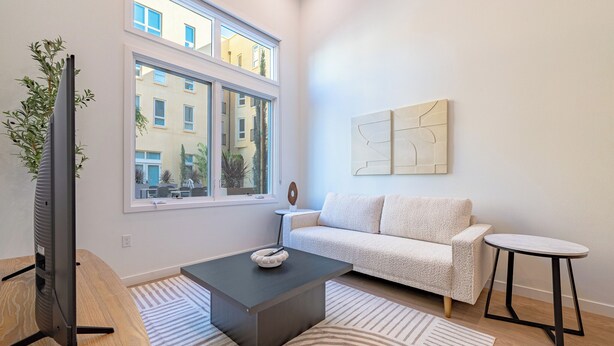 A modern living room with a sofa, a coffee table, a TV, and a window with a view of buildings.