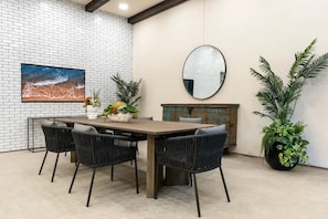 A dining area with a brick wall, a large painting, a round mirror, and potted plants. - Tranquil King 1B1B｜Pool & Spa｜Smart 4K TVs (Montclair)