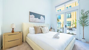 A bedroom with a bed, bedside tables, a window with a view, and a painting on the wall.