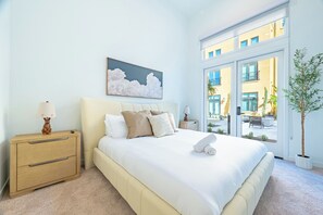 Un dormitorio con cama, mesitas de noche, una ventana con vistas y un cuadro en la pared.