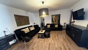 A modern living room with a black sofa, a dining table, and a TV mounted on the wall. - CASA DO PINHEIRO, near Olhos de Água River Beach and the Lake Azul (Pé de Cão)